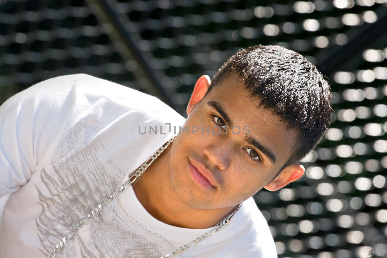 A young man standing in front of a chain linked fence in the city or at the basketball court.