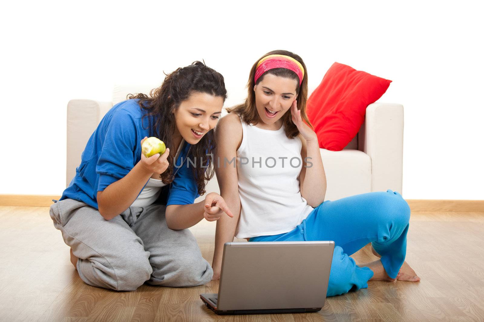 Two beautiful young women sitting on floor working with a laptop