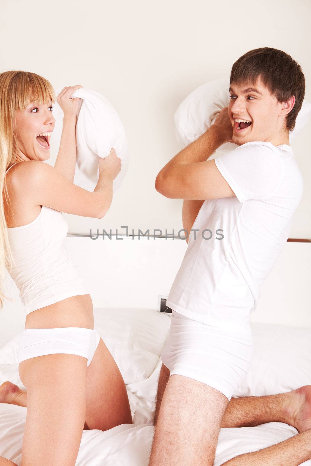 Young attractive couple emotionally pillow fighting on a bed