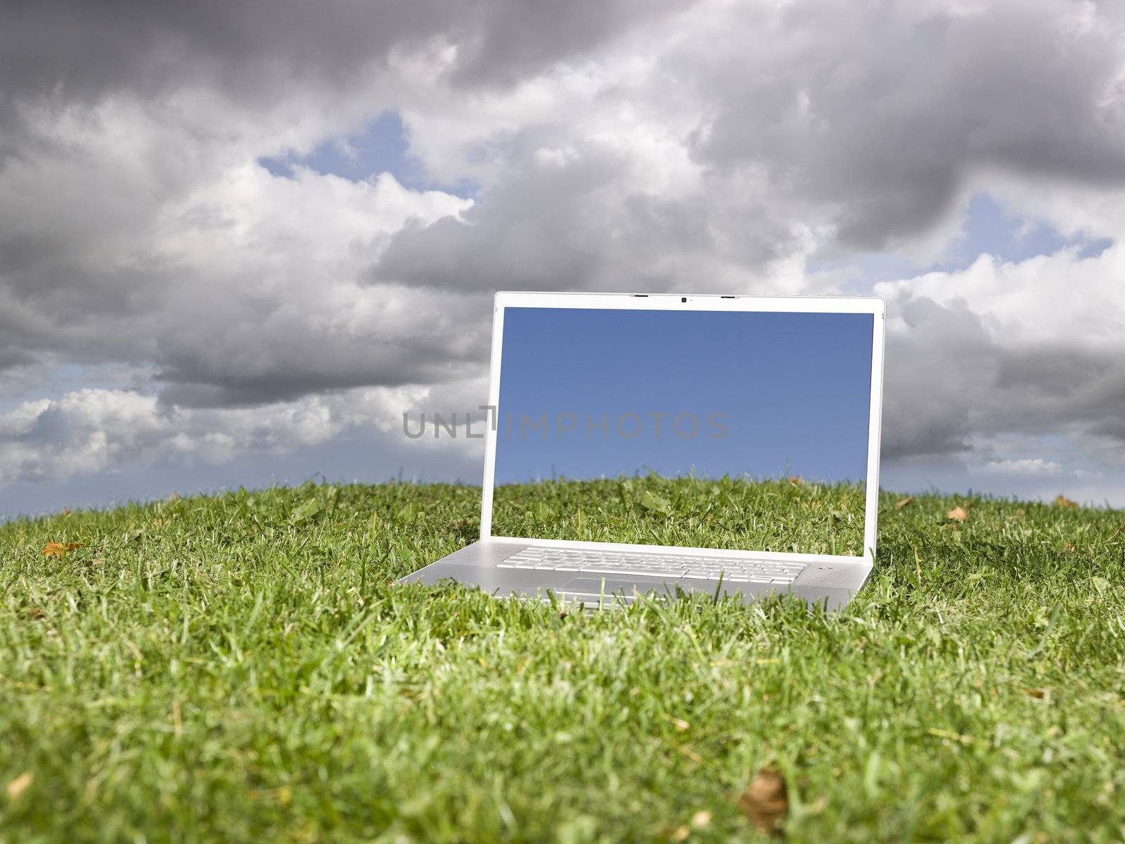 Laptop outdoors on a green field with a moody sky background