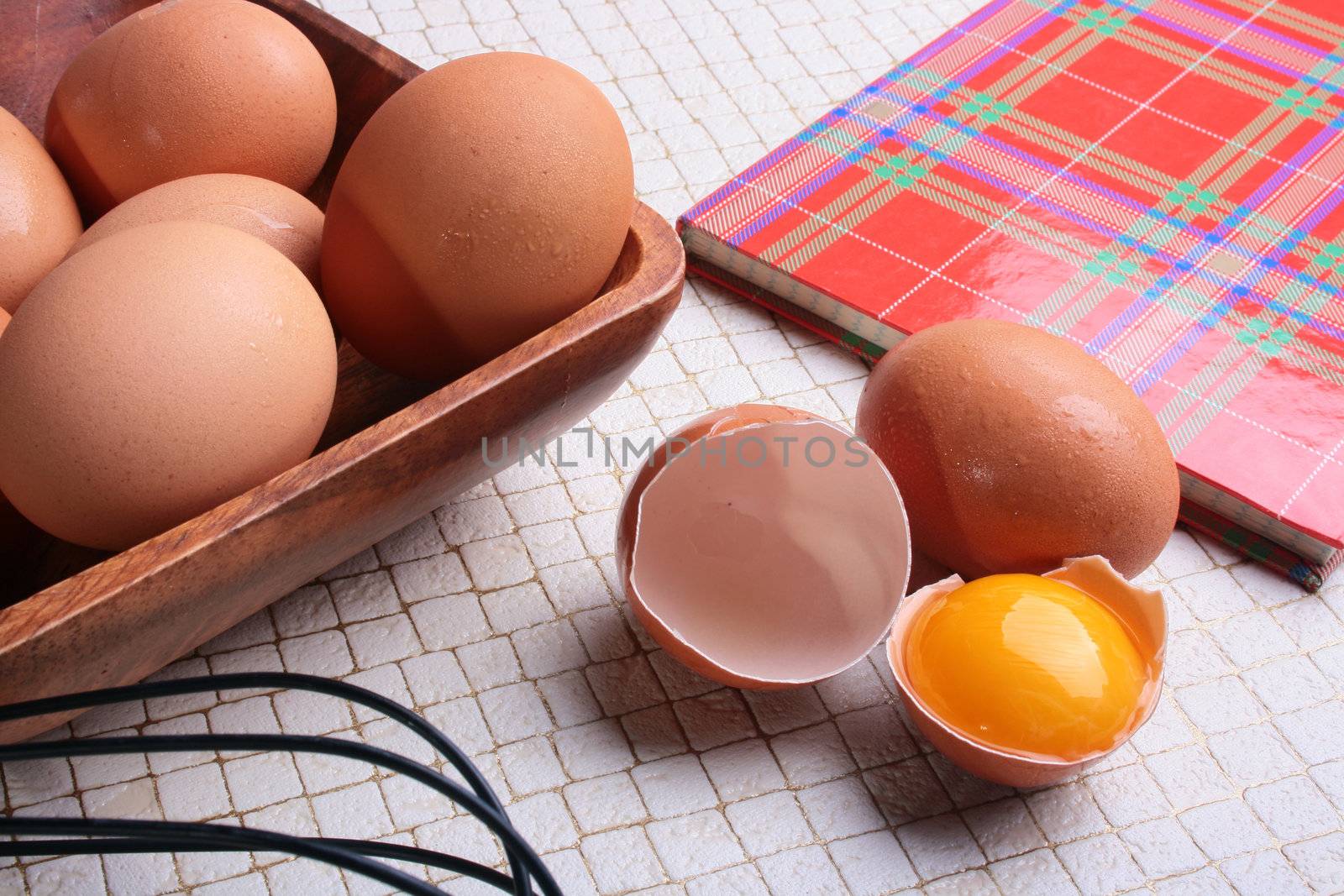 Book for recipes on a kitchen table with eggs and a beater.