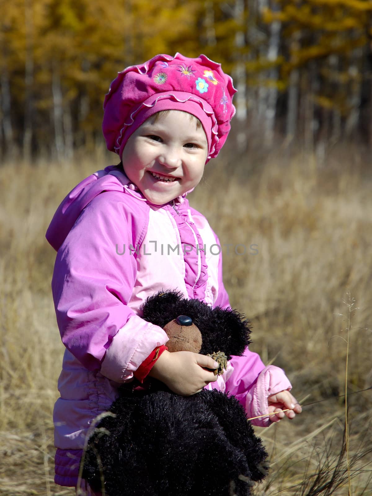 Little girl in pink suit holding teddy bear in her hand