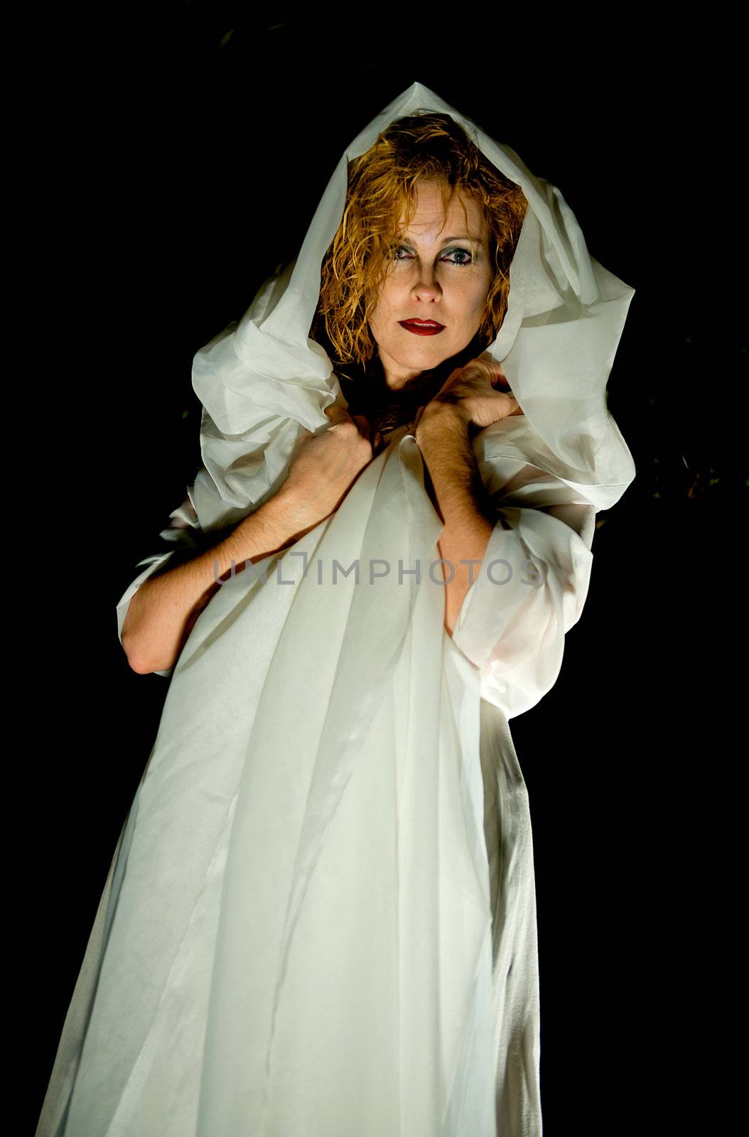 Mysterious image of attractive blonde woman wrapped in white cloth in the dark of night.  Image has a somewhat eerie yet spiritual feel to it.
