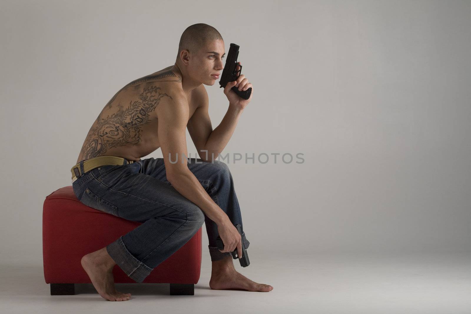 A young, muscular brazilian man in a studio shot, on a red seat, on a gray background.