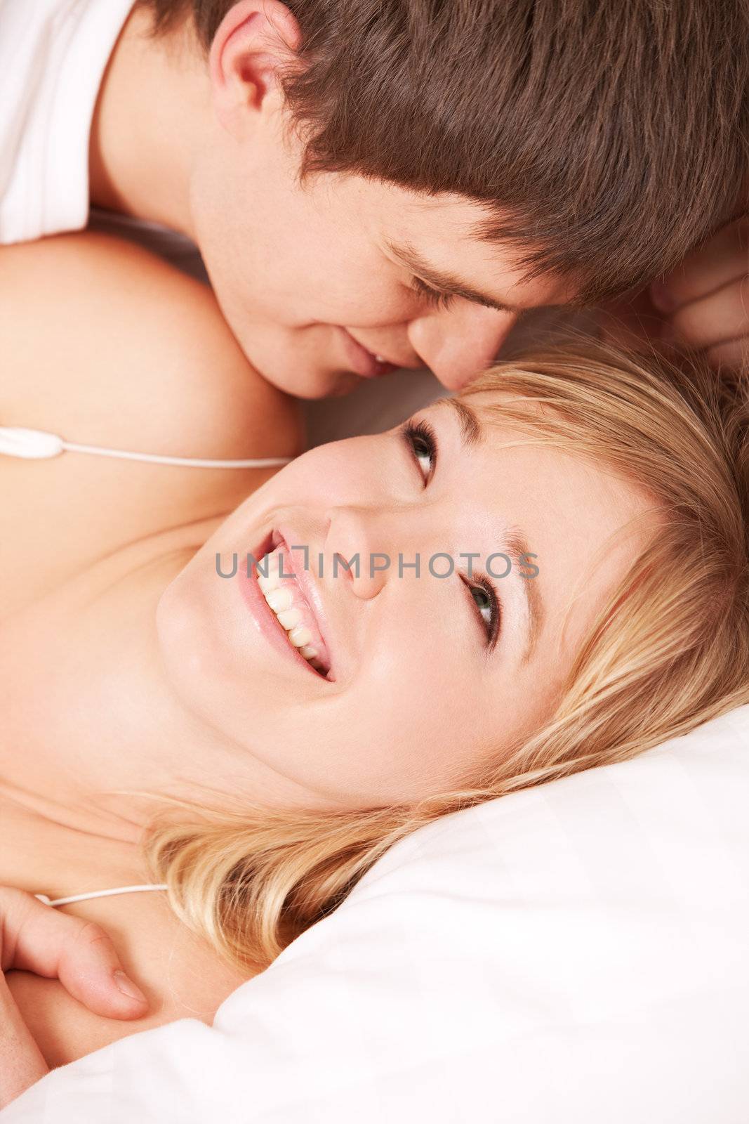 Young smiling couple in a bed on white sheets