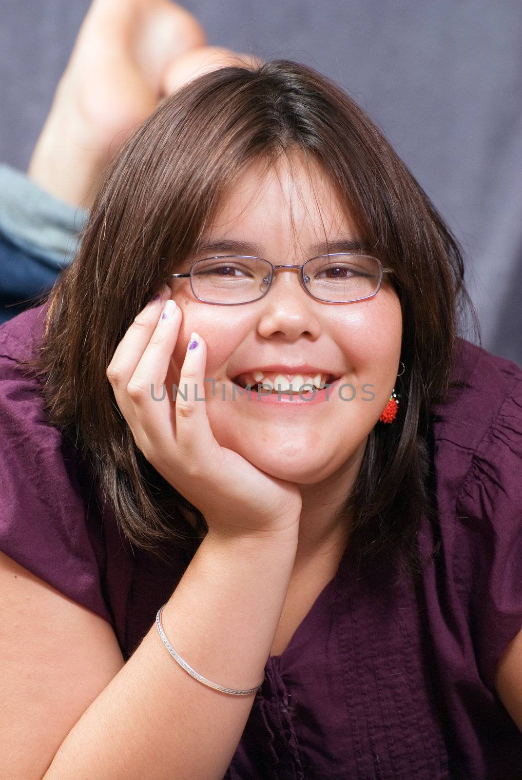 A 10 year old girl lying down and leaning on her elbow, smiling at the camera