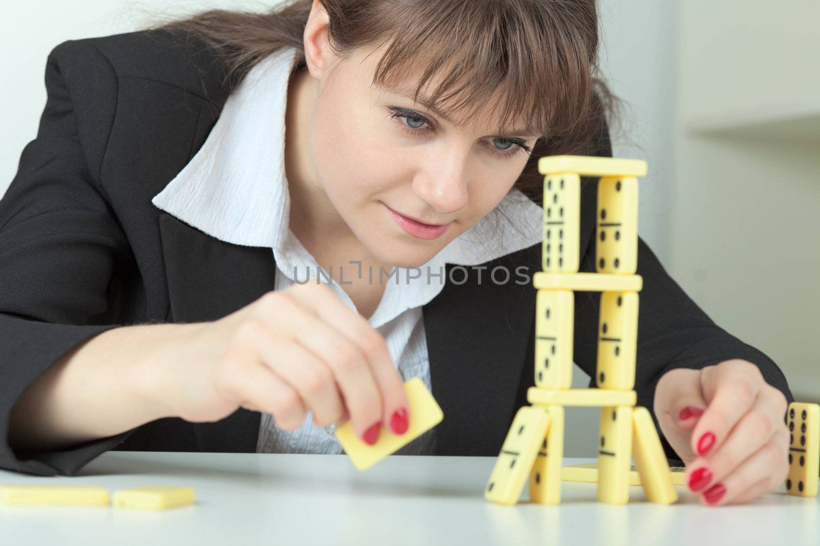 Young woman builds tower of dominoes bones on table by pzaxe