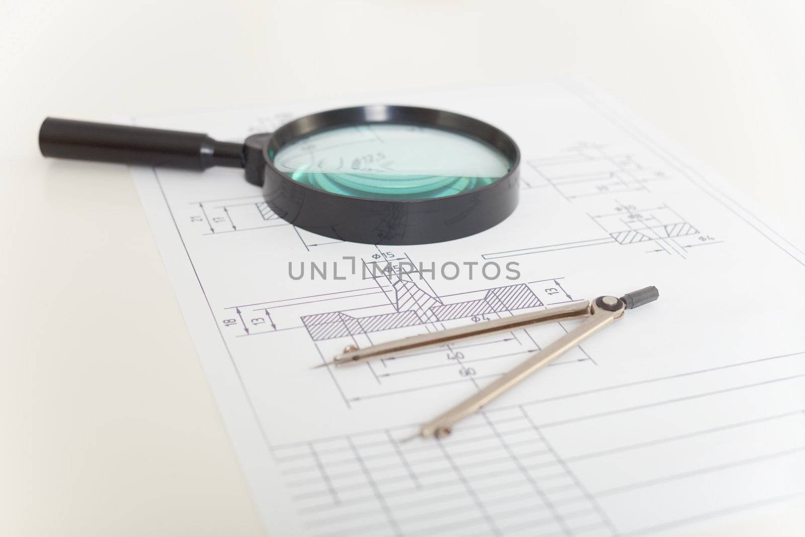 The drawings, magnifier and compasses on a white table