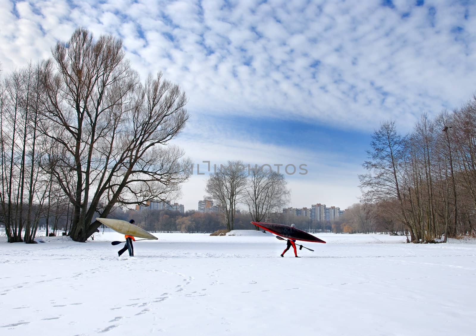 Two oarsmen with oars and kayaks go on ice of the frozen lake.