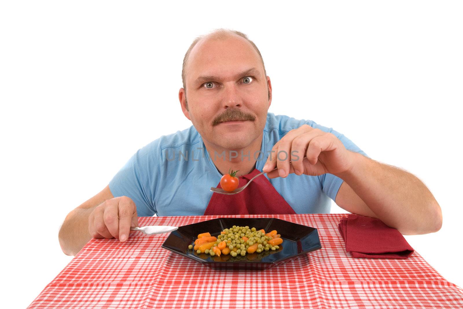 Mature man sitting with a plate full of vegetables and a tomato on his fork