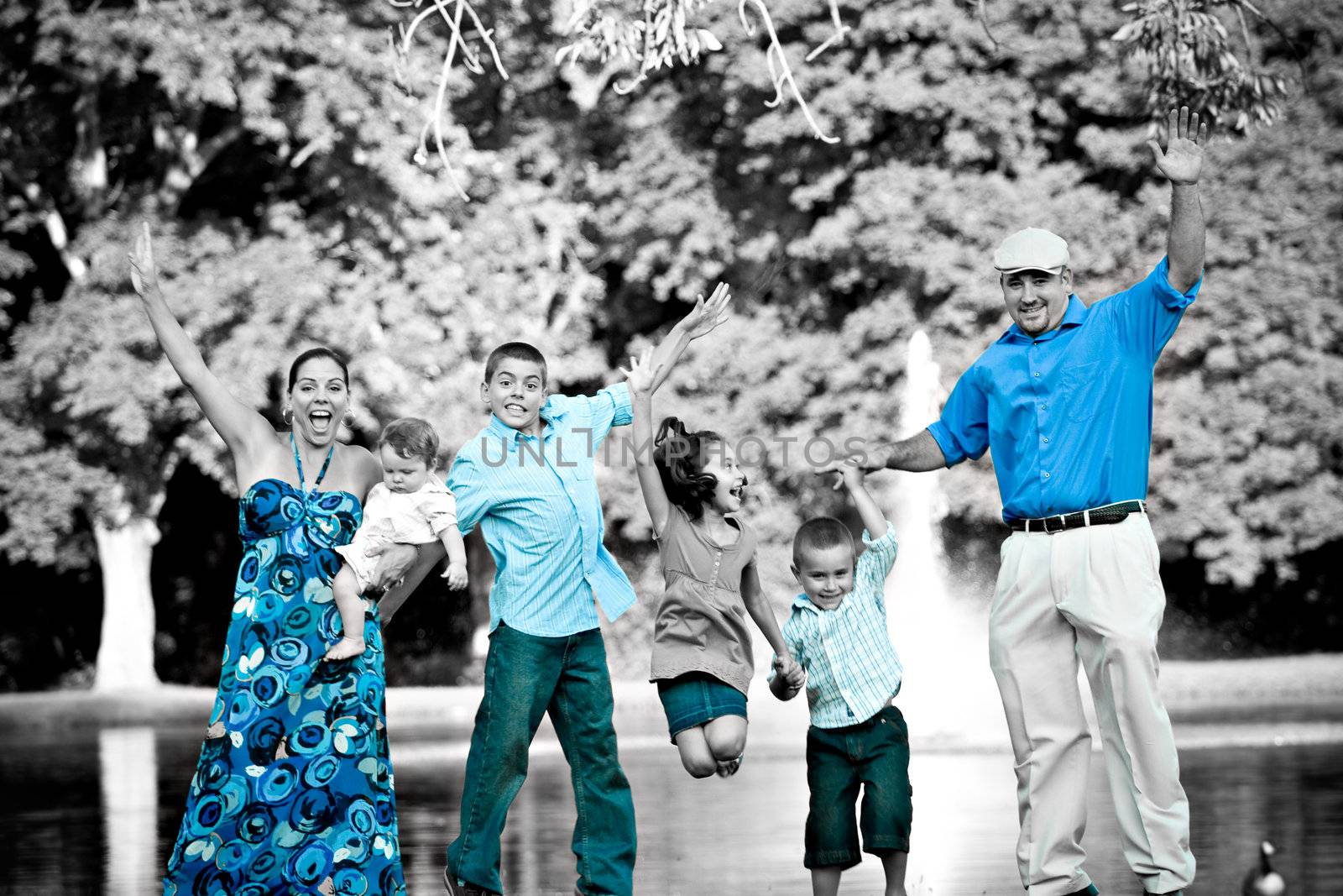 Portrait of a fun young family with four children jumping in the air all at once.  Selective isolated color highlighting the blues.