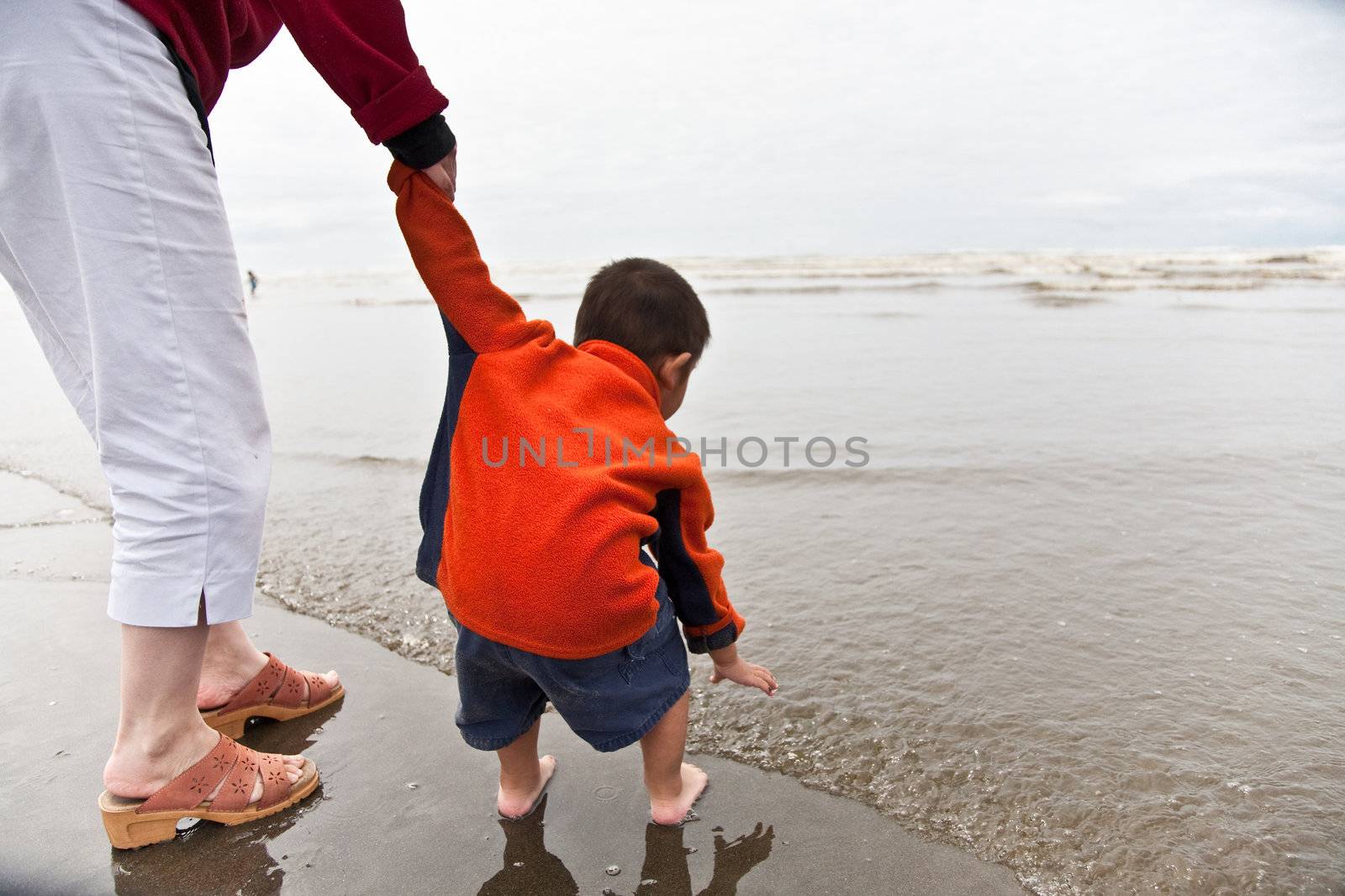 A mother holding her son's hand walking on the beach