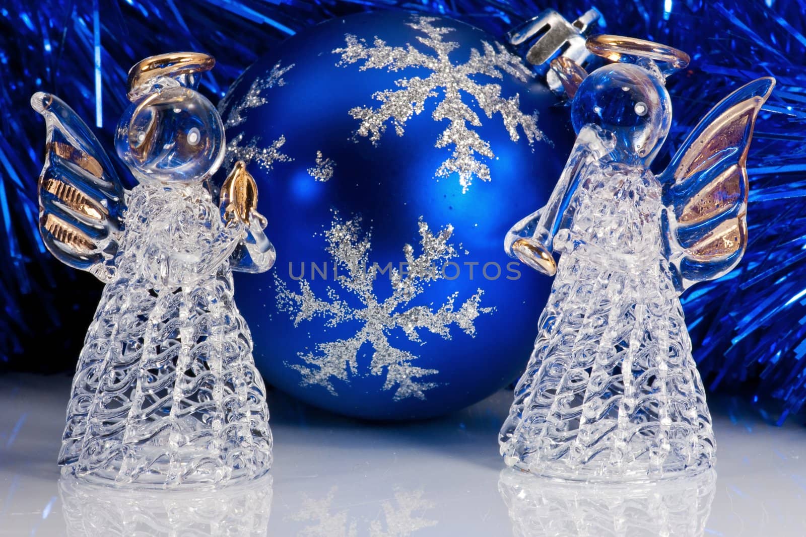 Two decorative glass angel, blue christmas ball and Christmas tree tinsel on white with reflections