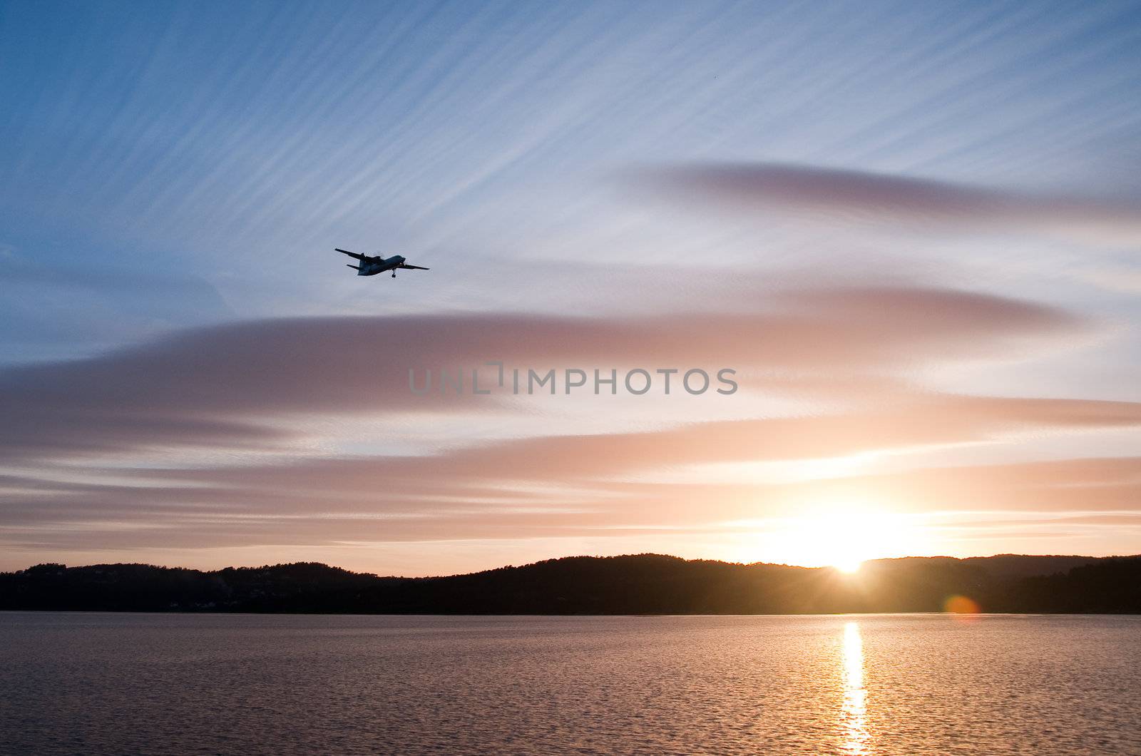 Airplane in the sunset over the water with blue sky and hills in the background