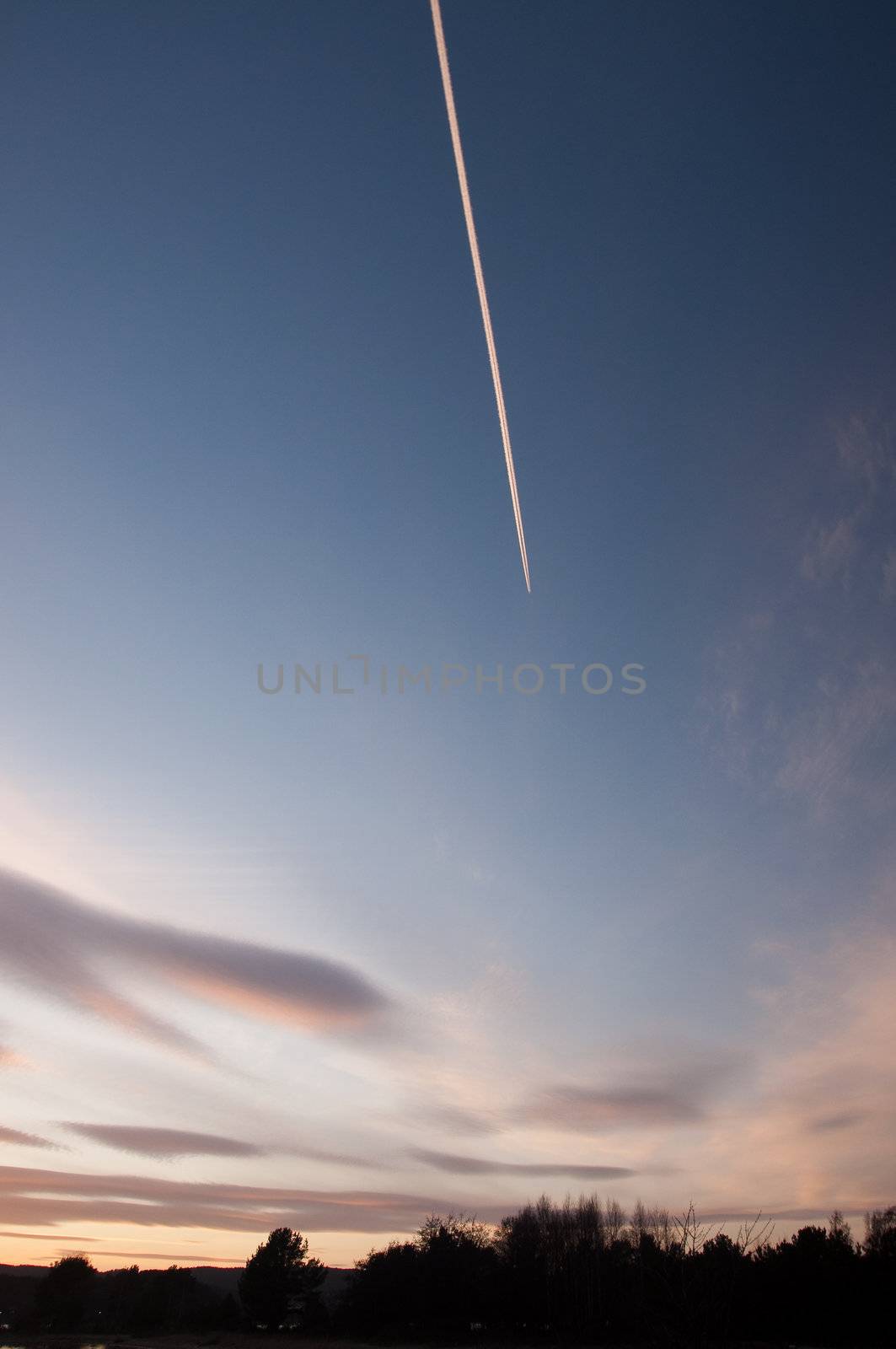 Airplane flying high leaving a contrail on a blue sky at sunset
