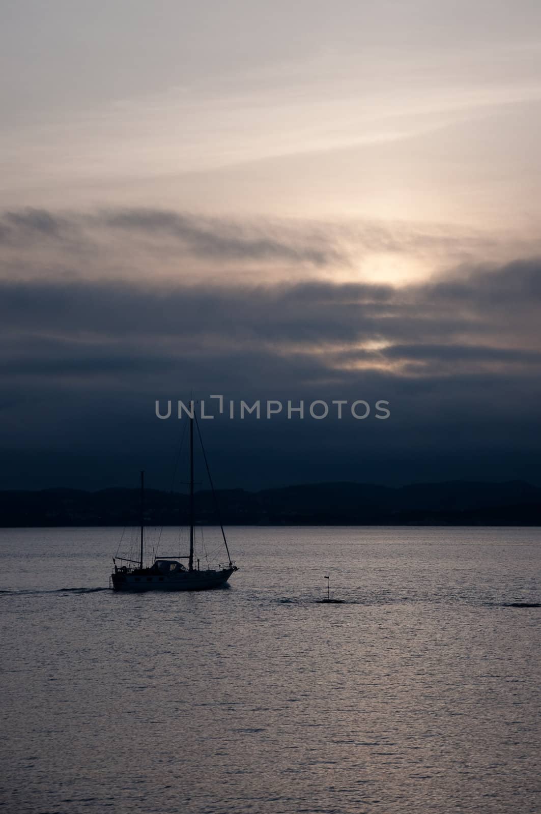 Sailboat in dark sunset with hills in the background