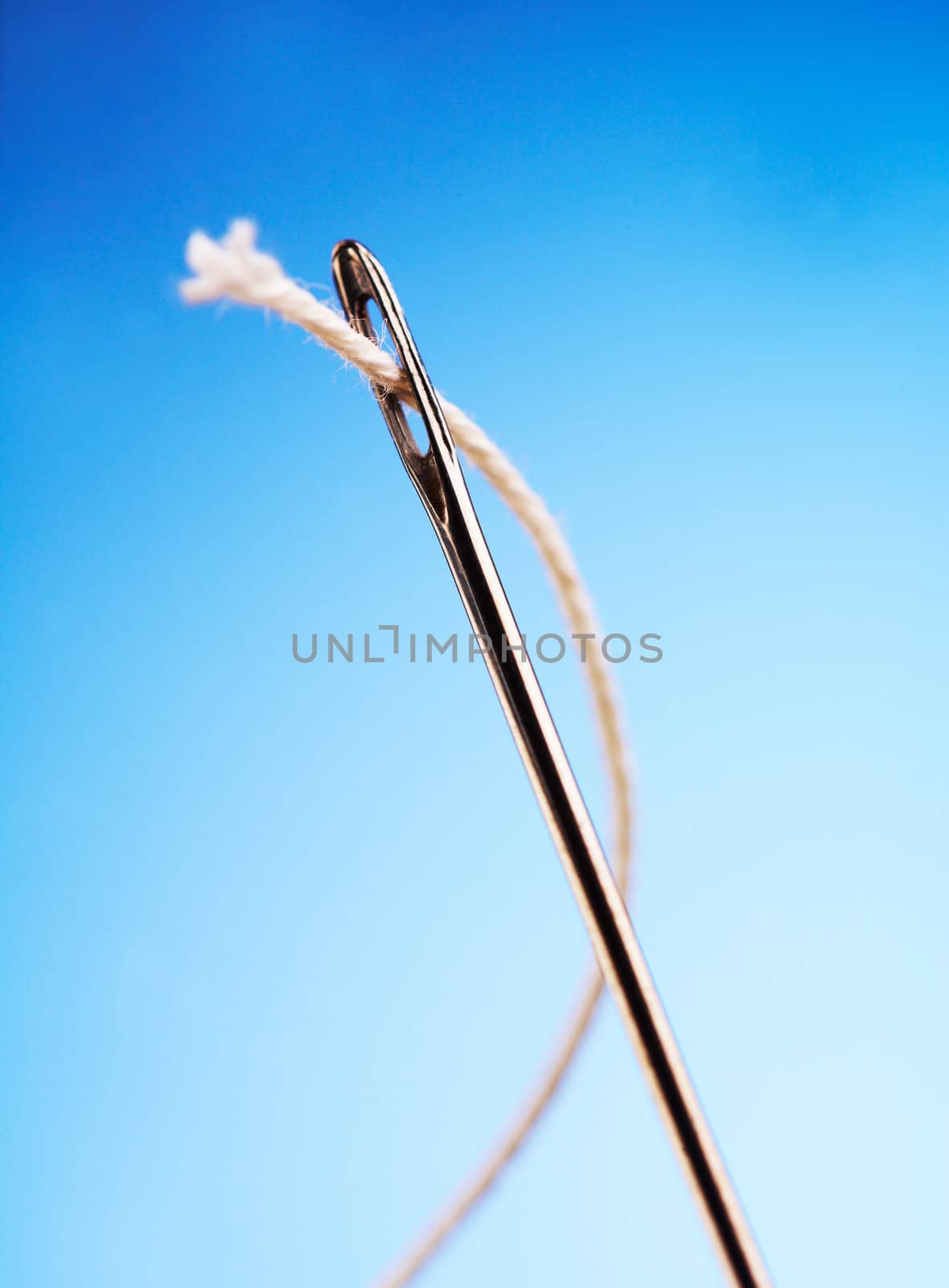 White thread going through needle eye closeup on blue background