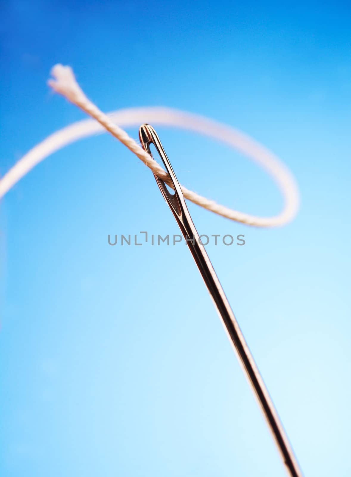 Thread passing through needle eye, close-up on blue background