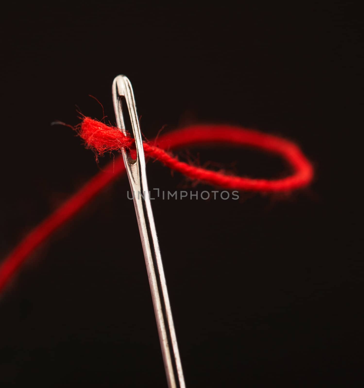 Red thread going through needle eye, closeup