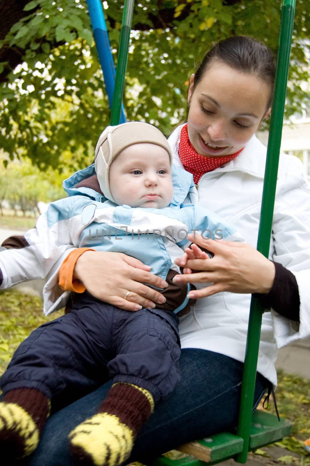 Young mother and baby boy on swing in autumn park