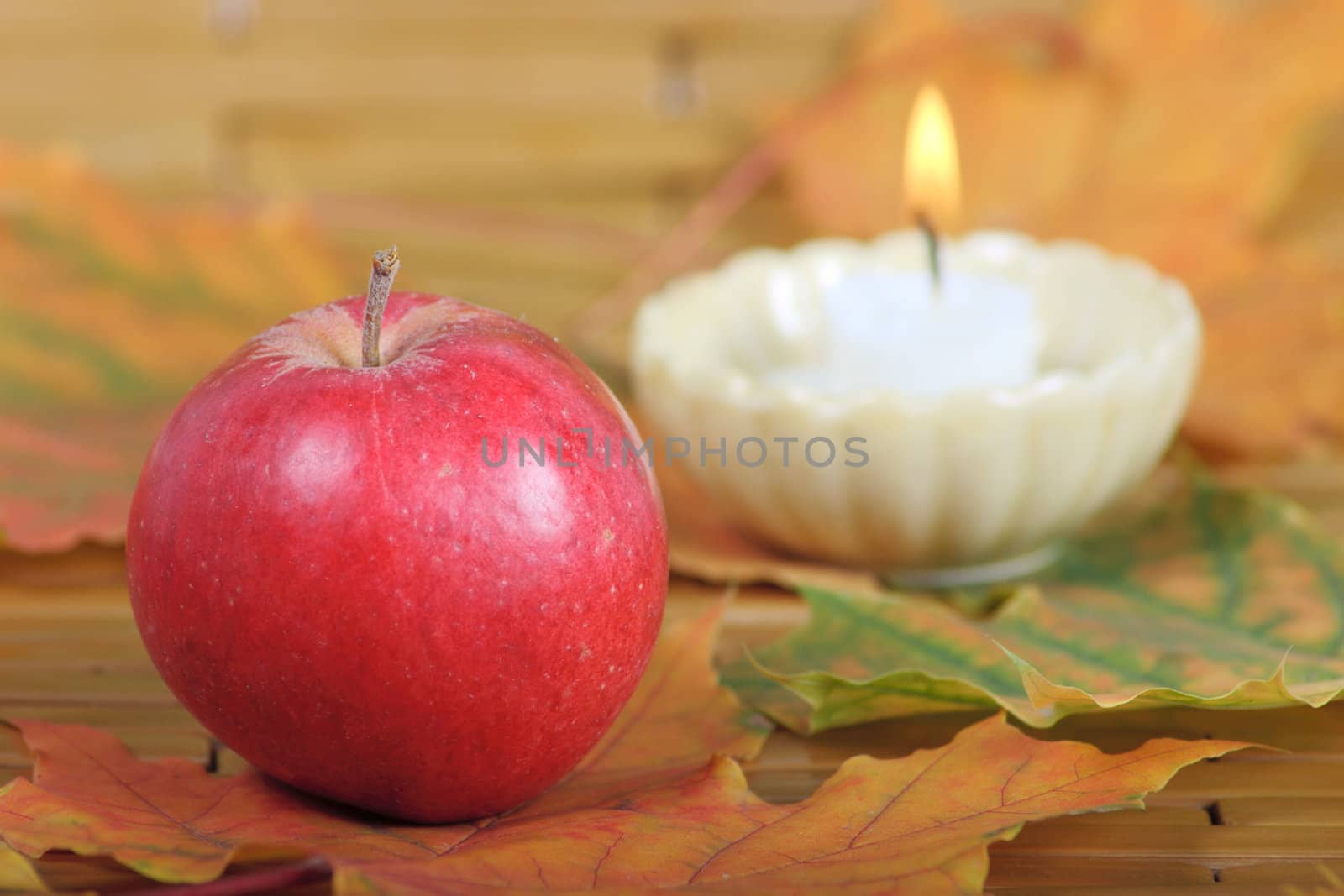 Red apple on autumn leaves with burning candle on a background