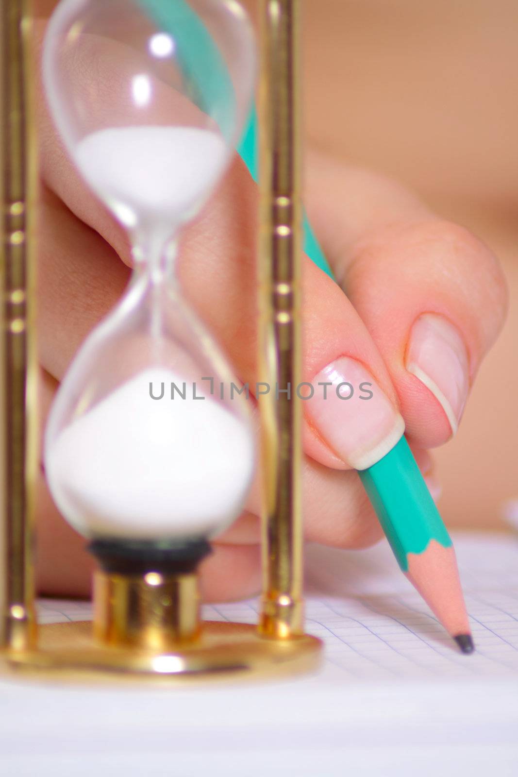 Female hand with a pencil and a sand clock removed close up