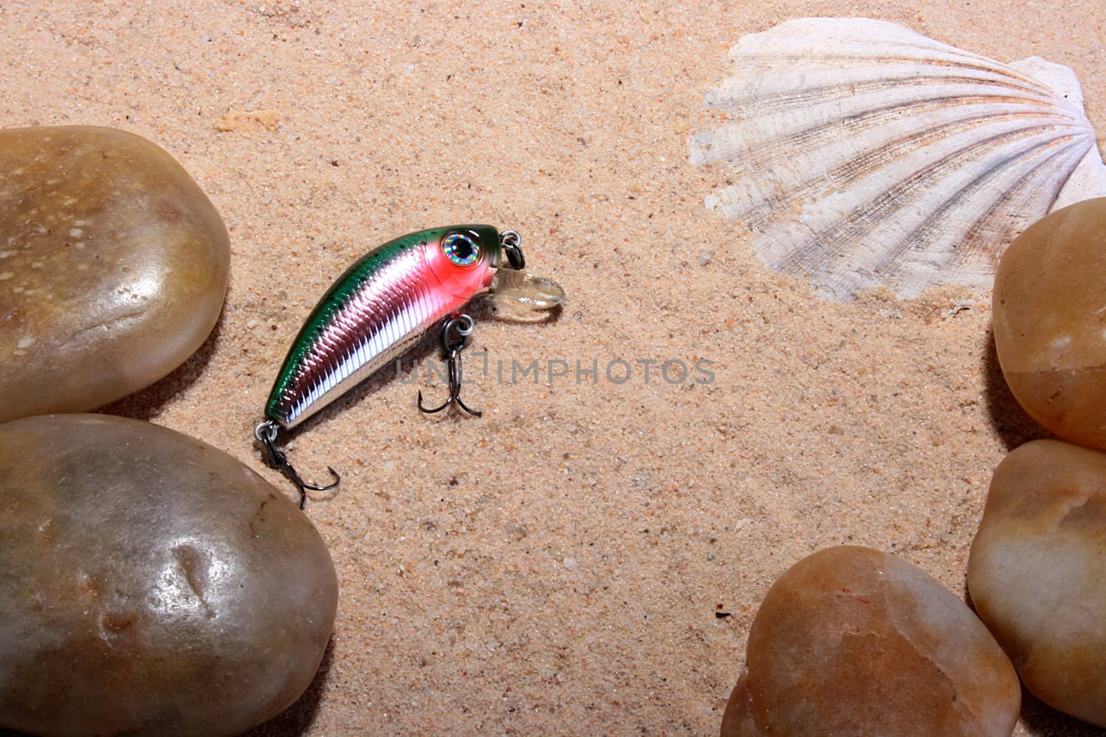 Artificial small fish - a bait for fishing in the rivers, the seas and lakes on sand with a cockleshell and pebbles.