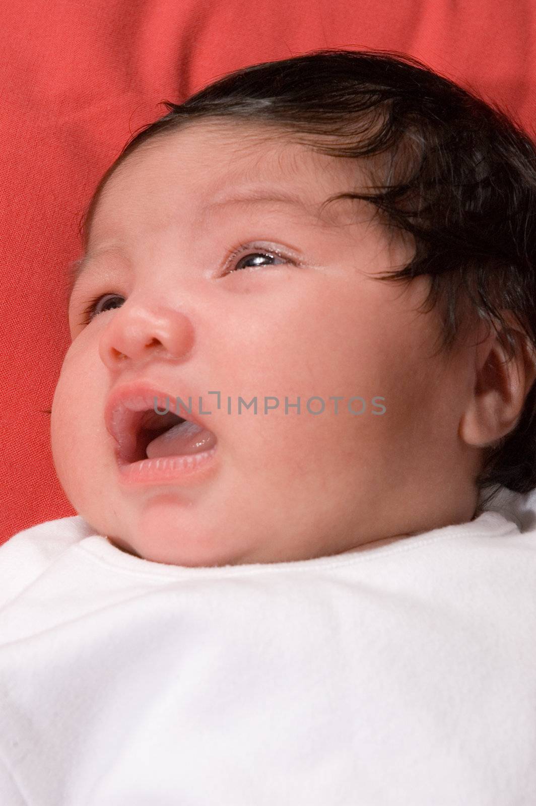 multiracial baby laying on red blanket awake