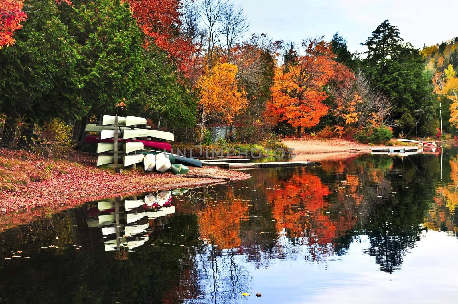 Canoes at forest of colorful autumn trees reflecting in calm lake