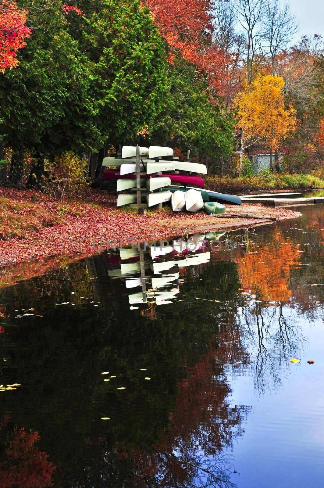 Canoes at forest of colorful autumn trees reflecting in calm lake