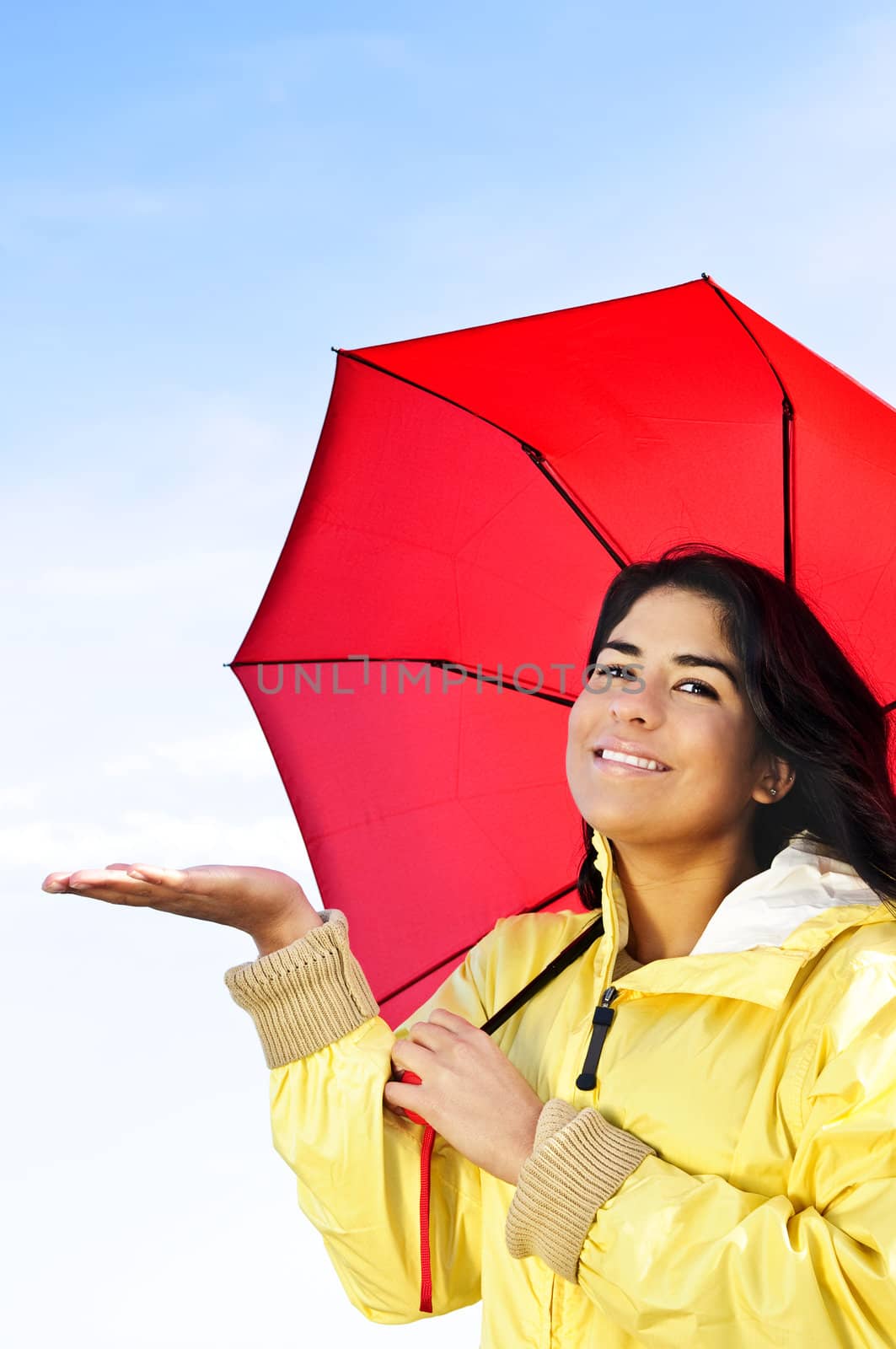 Portrait of beautiful smiling girl wearing yellow raincoat holding red umbrella checking for rain