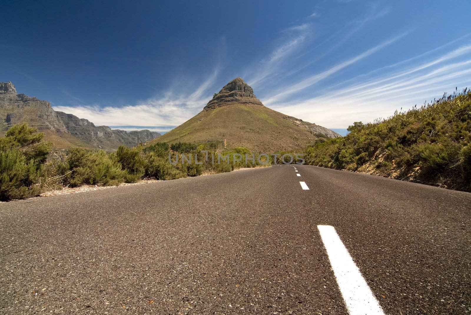 Road leading toward a mountain in the background with blue sky and clouds