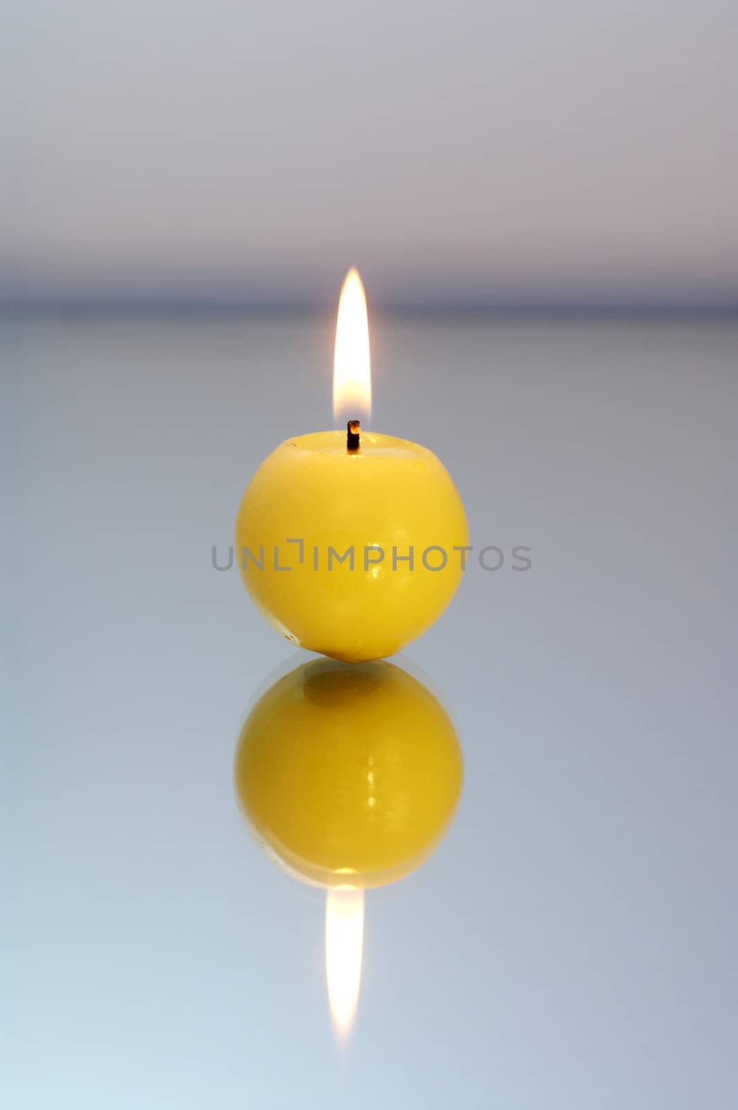 Round yellow candle burning on a reflective surface.