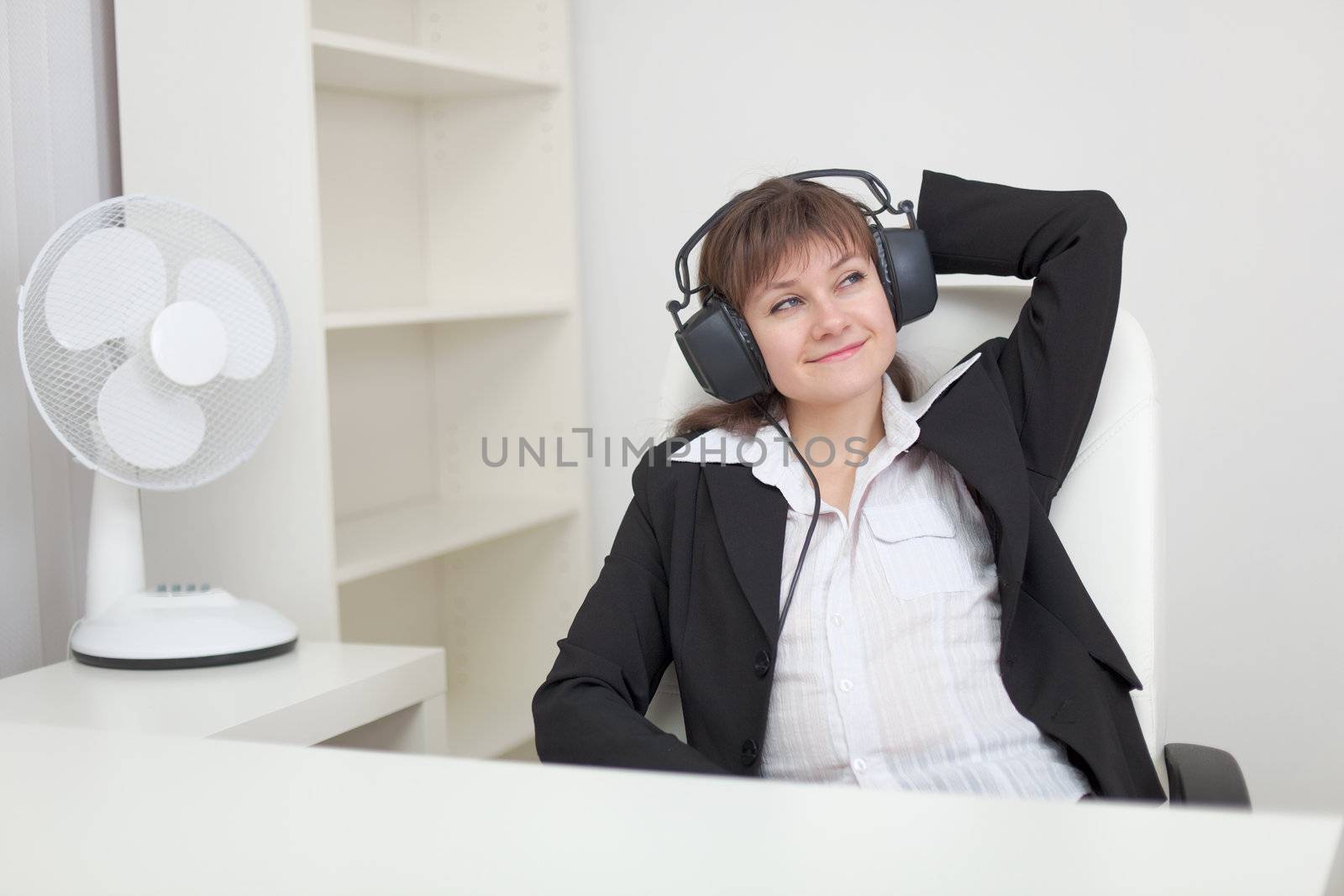 The woman sits in an armchair and listens to music in the big ear-phones