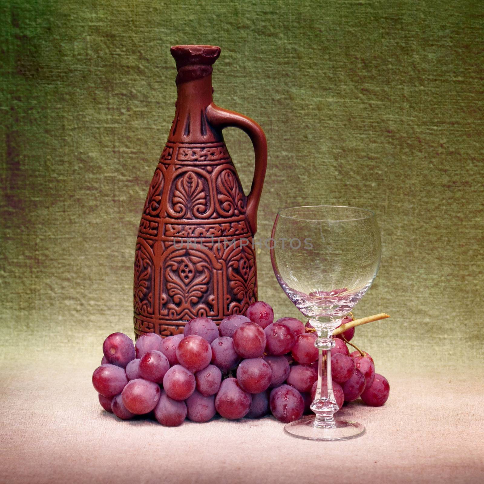 Still-life with a clay large bottle, a glass and grapes against a canvas