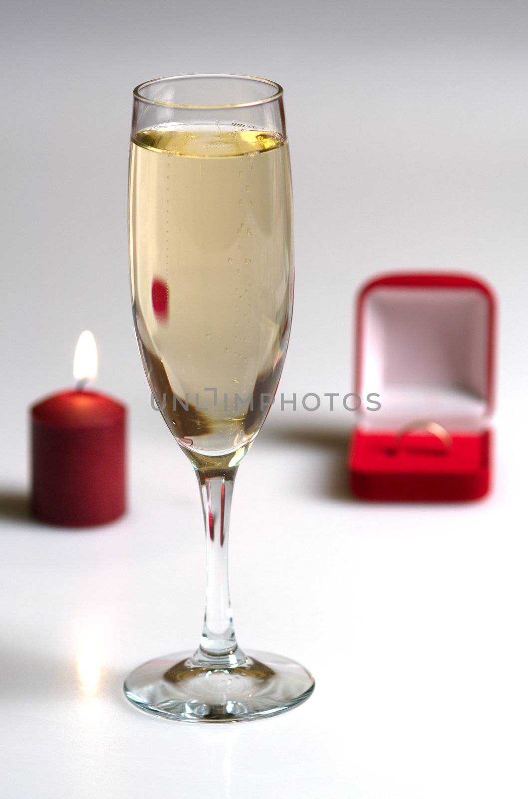 Candle, box with a gold ring and a champagne glass.