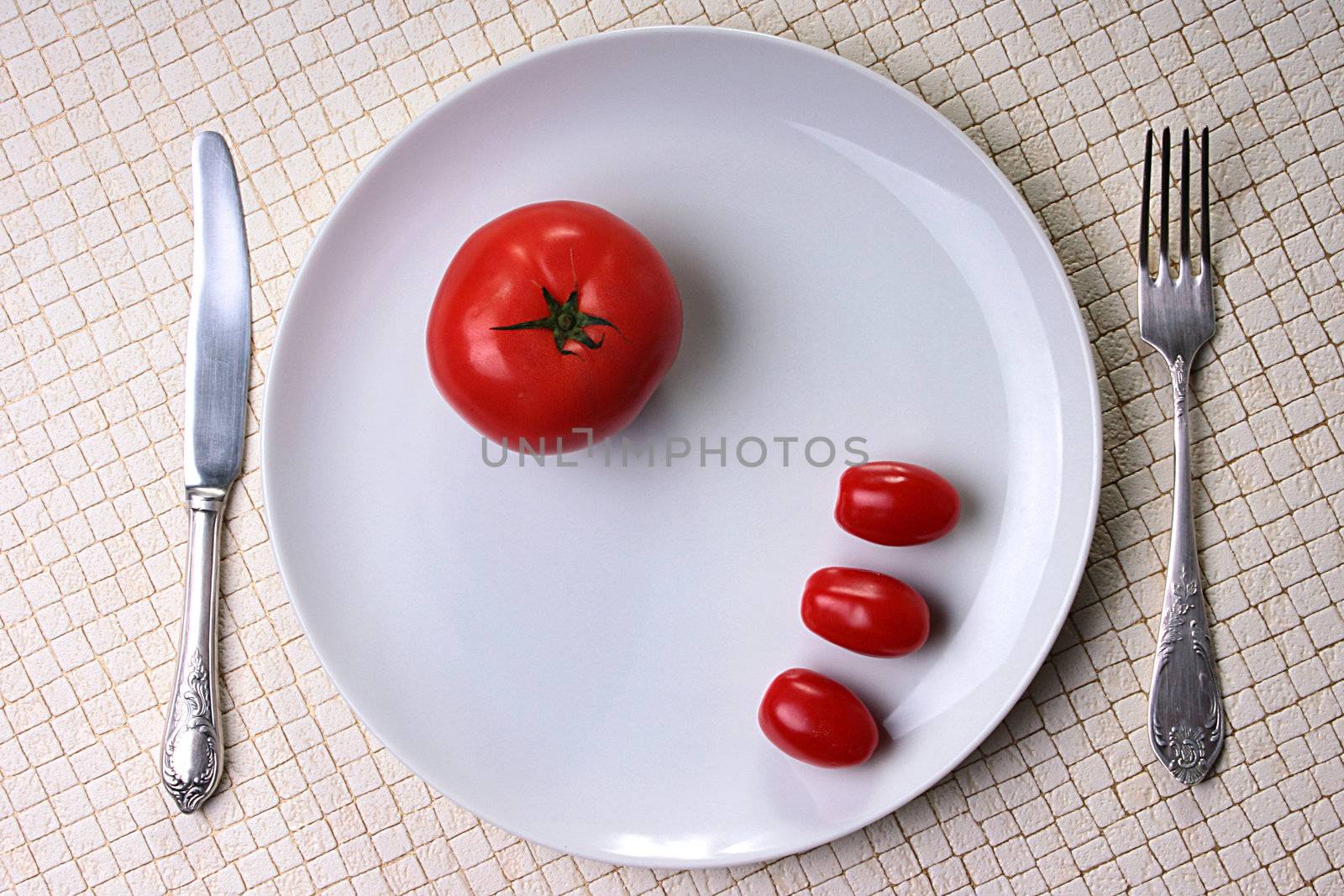 Three small and one big tomato on plate with fork and knife.