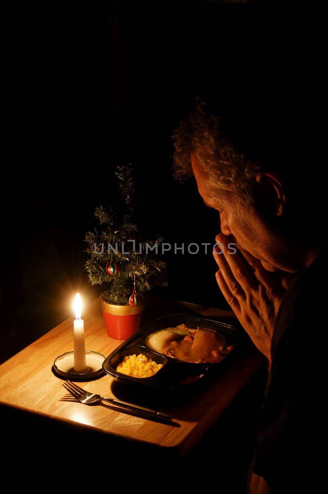 A lonely man praying over a TV dinner at Christmas.