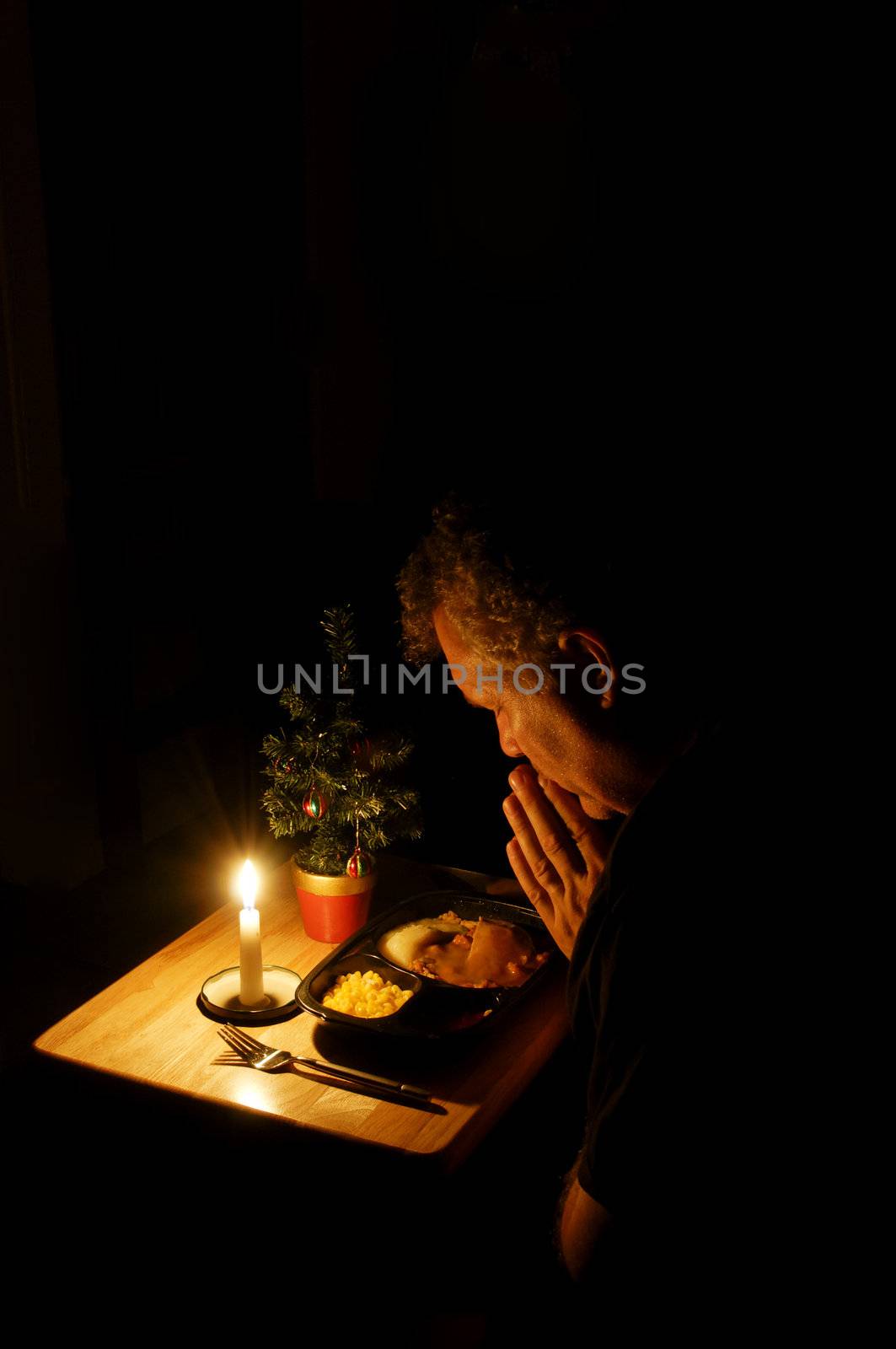 A middle-aged man praying over a TV dinner at Christmas time.