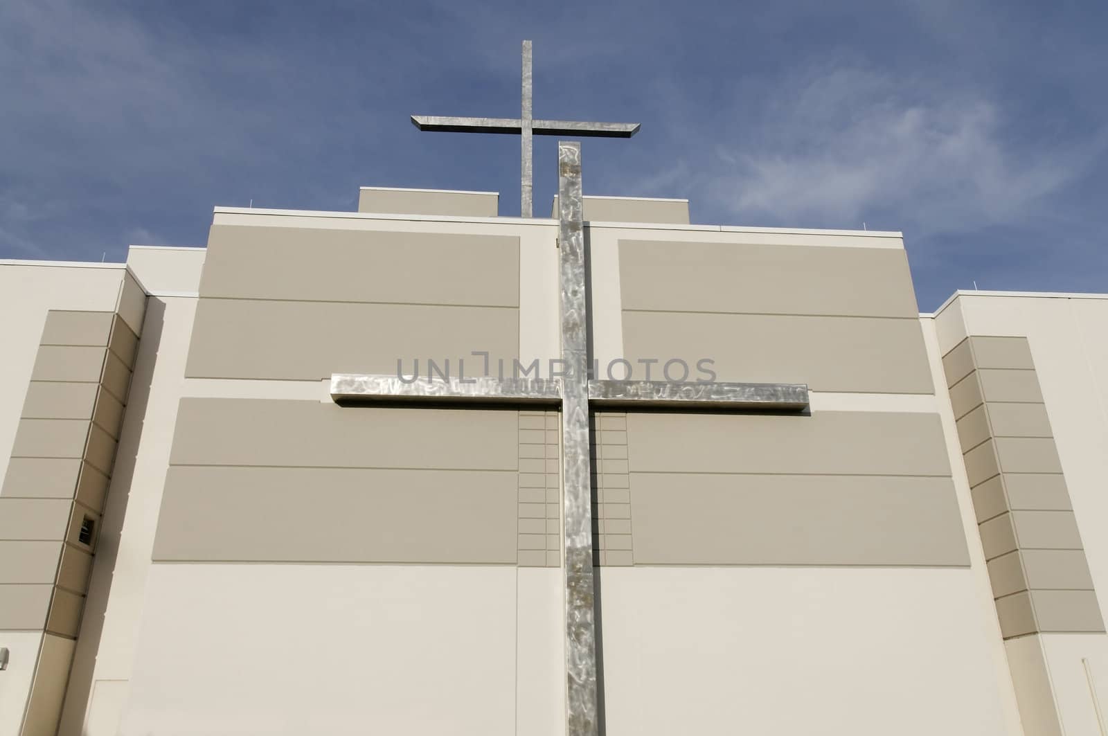 A modern church with two crosses on it with a blue sky above.