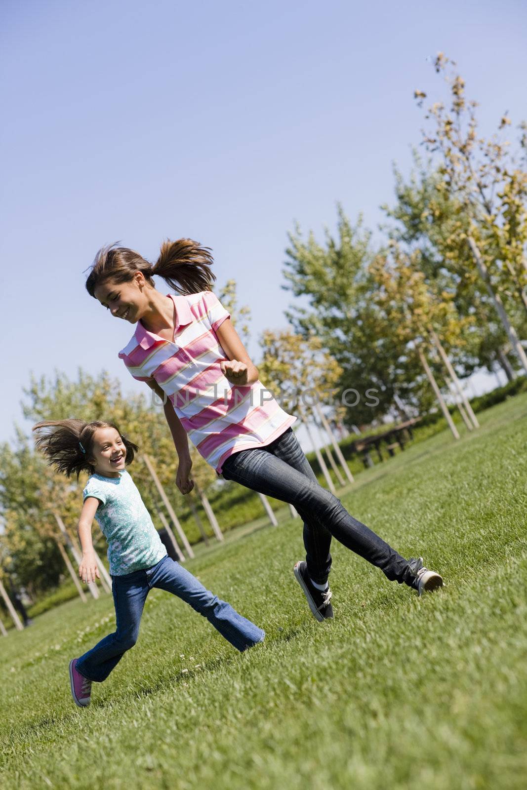 Two Hispanic Sisters Running on Grass in Park