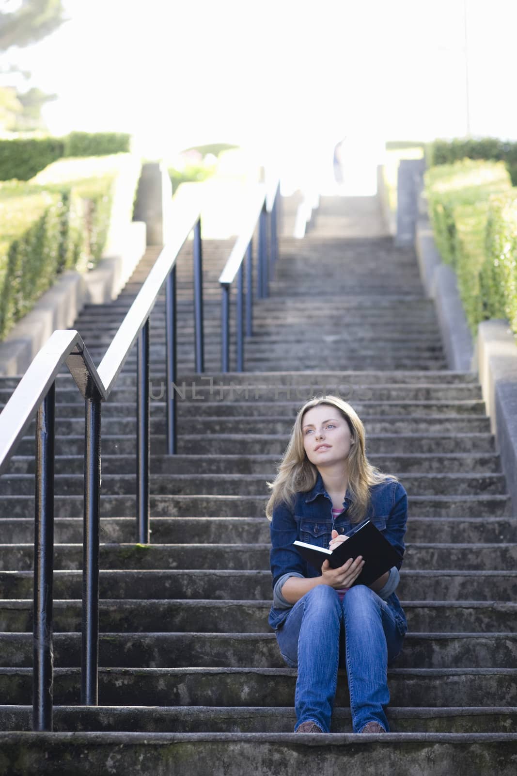 Pretty Blonde Teen Girl Sitting at Bottom of Stairway Writing in Journal