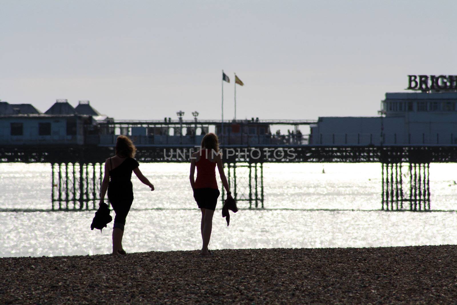 Two young female teens walking on the beach of Brighton at sunset.