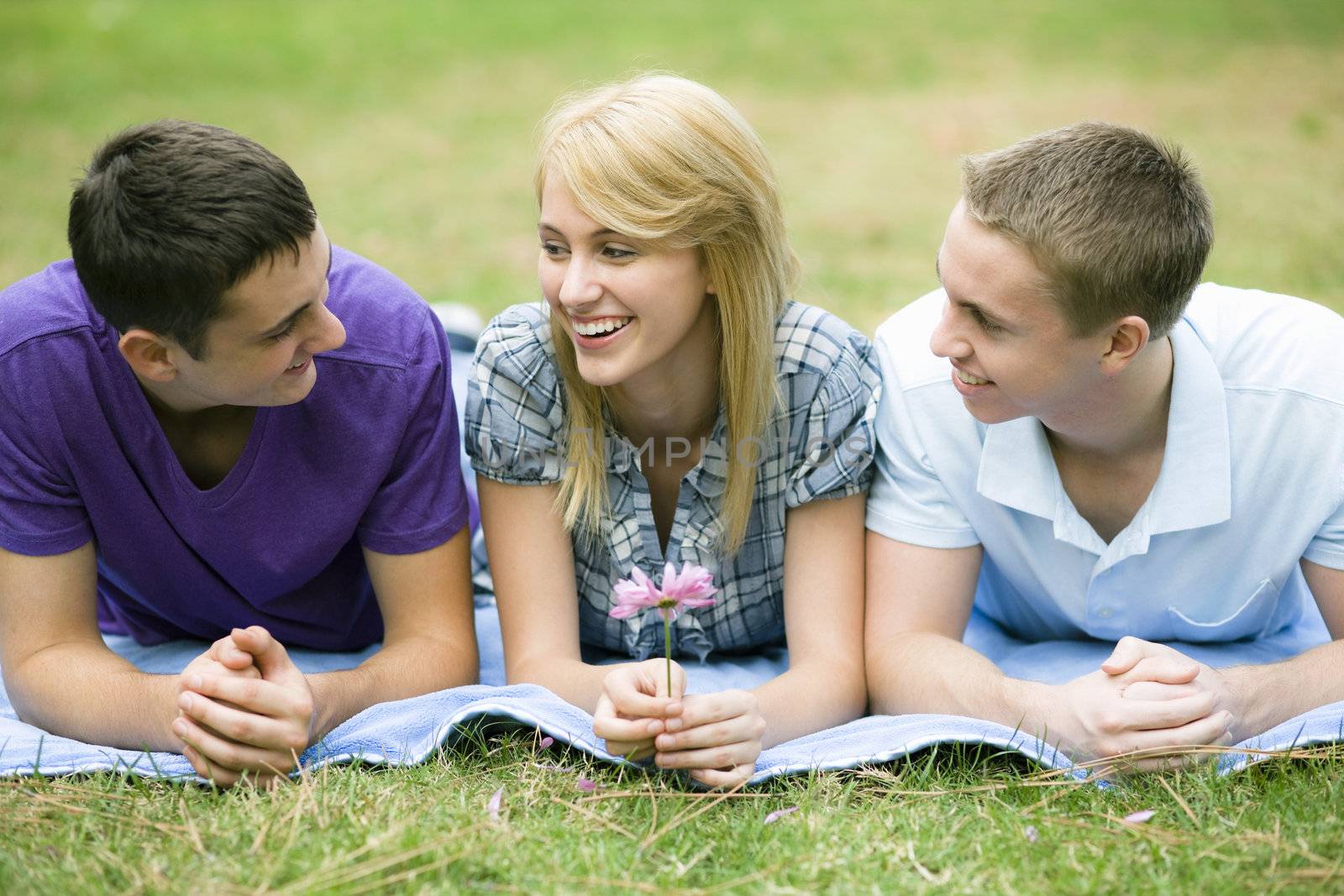 Three Smiling Teens Lying on Blanket in a Park