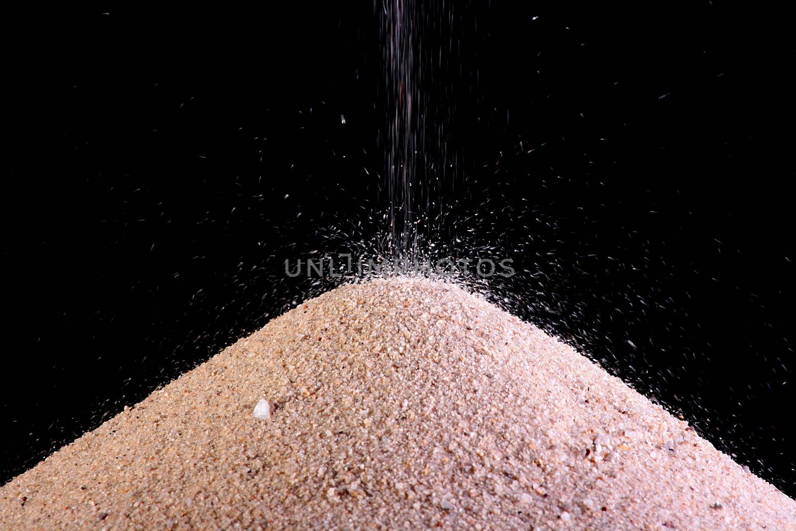 Heap of river sand on a black background on which sand continues to be strewed.