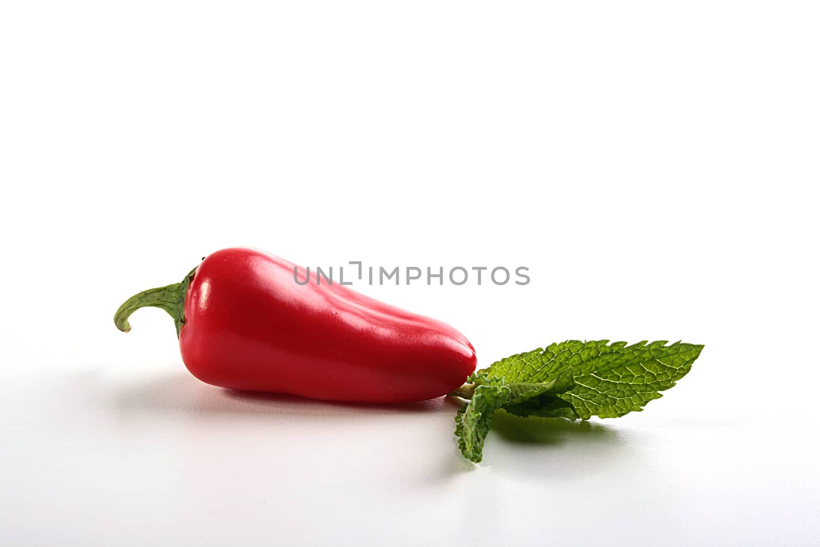 Hot red pepper with a basil leaf on a white table.