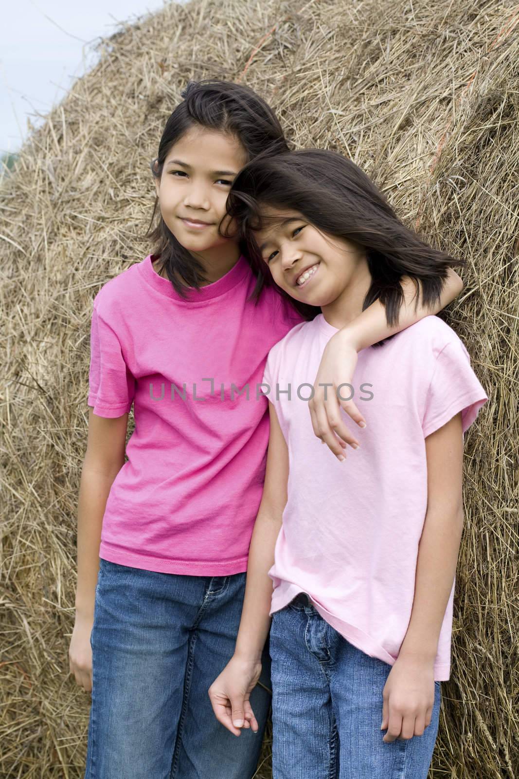 Two young girls standing against haybale