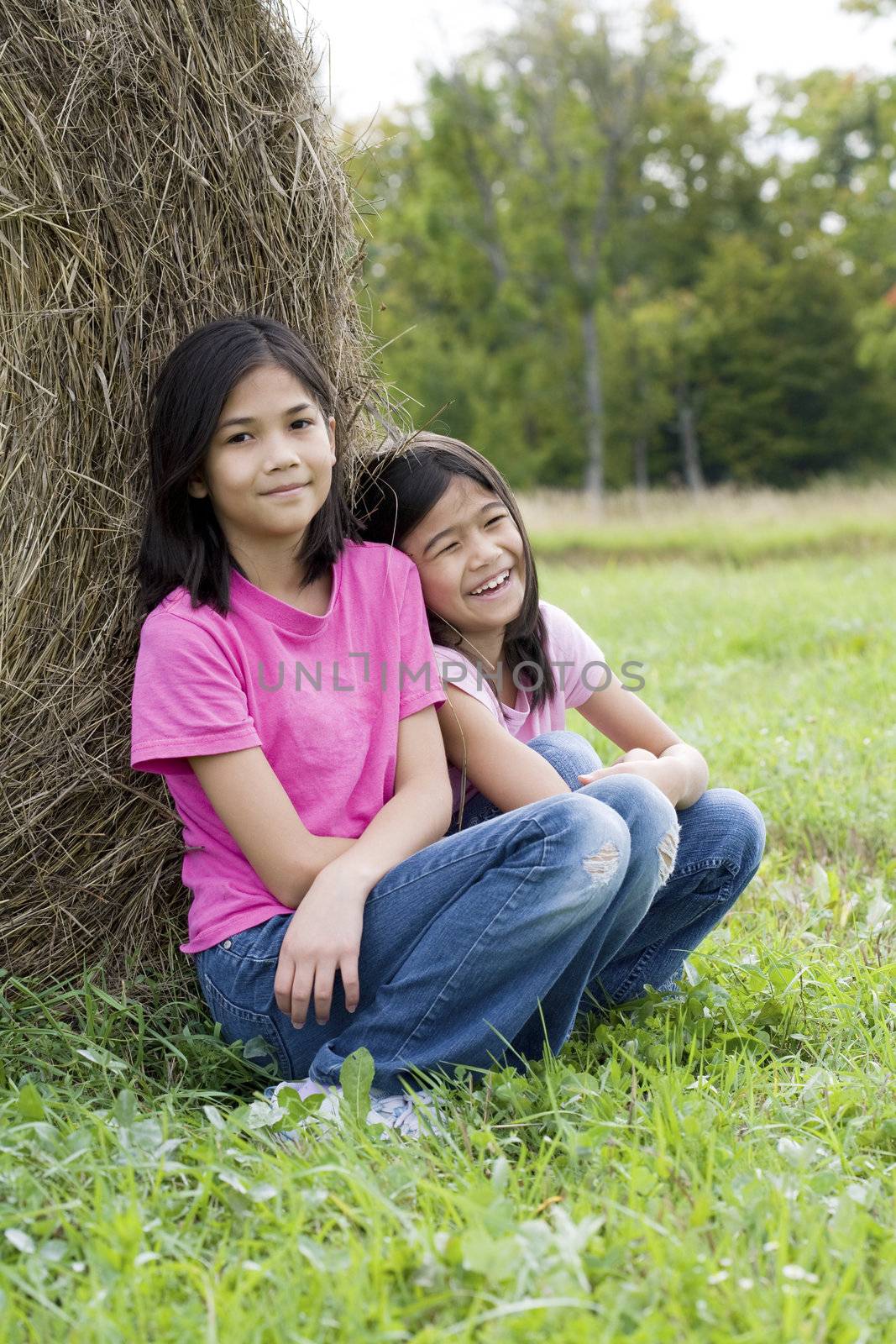 Two young girls sitting against haybale  by jarenwicklund