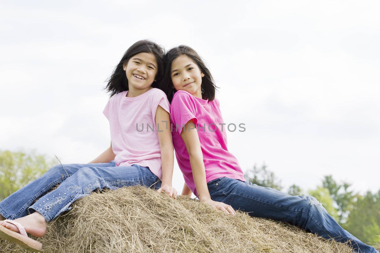 two young girls sitting on top of haybale by jarenwicklund