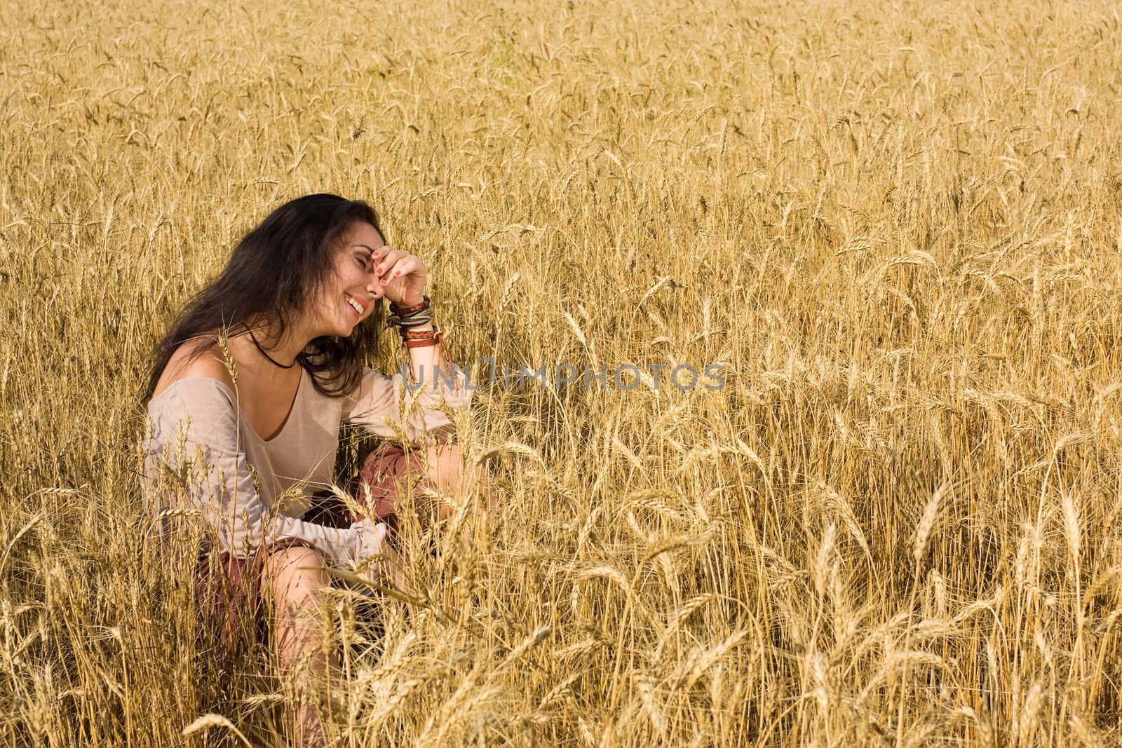 Attractive girl sitting in golden wheat by rozhenyuk